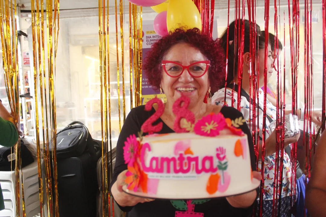 Mulher sorri exibindo um bolo com velas "28" e o nome da Camtra