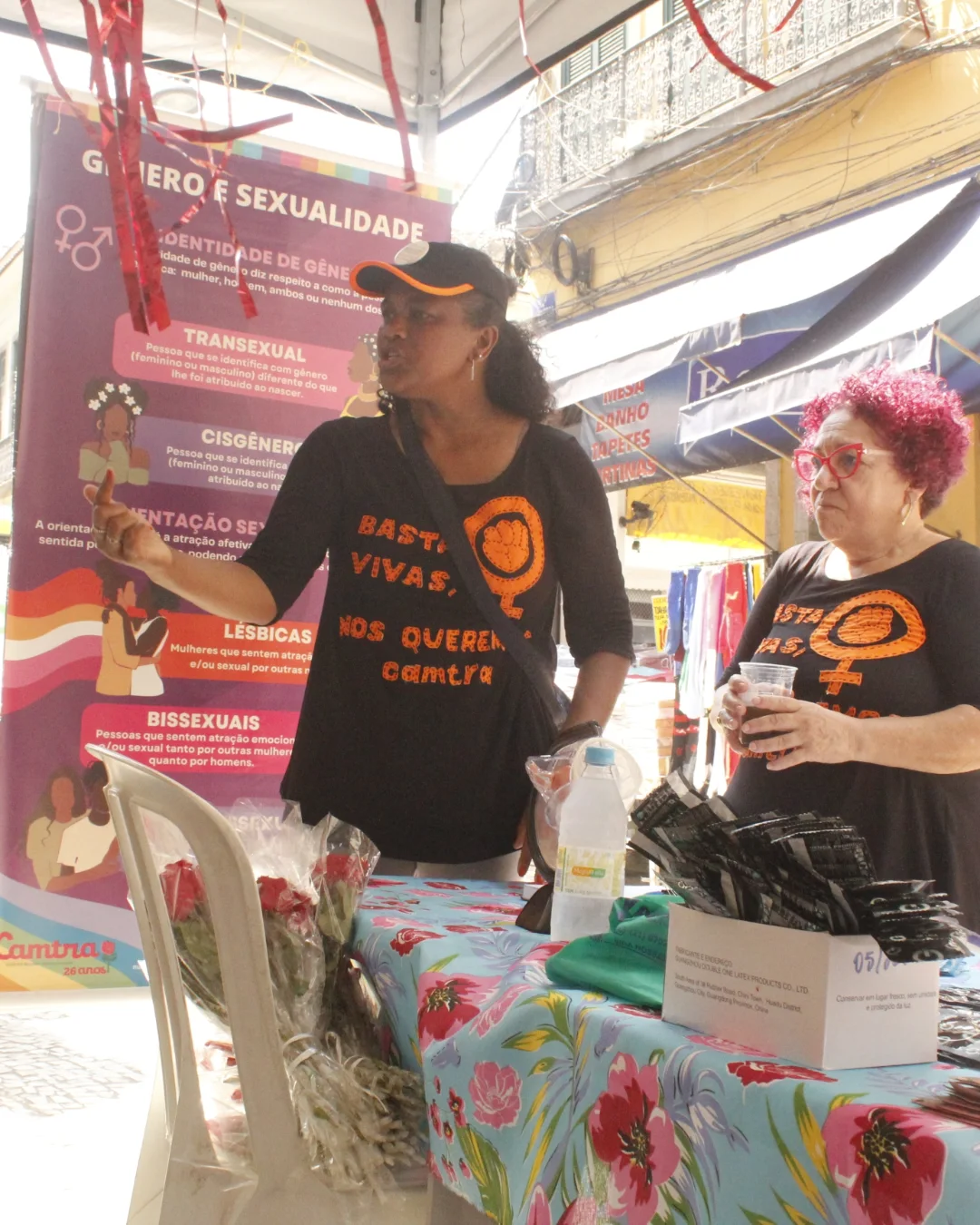 Duas mulheres com uniformes da Camtra entregam rosas para mulheres na Saara